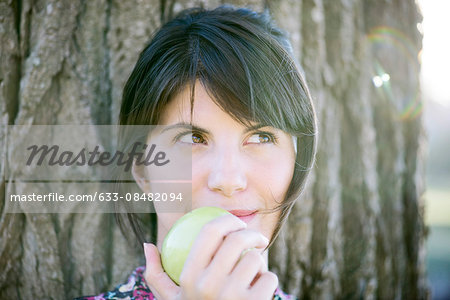 Woman eating apple, looking up thoughtfully