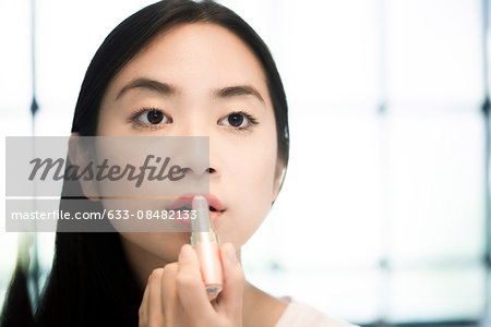 Woman looking in mirror, applying lipstick