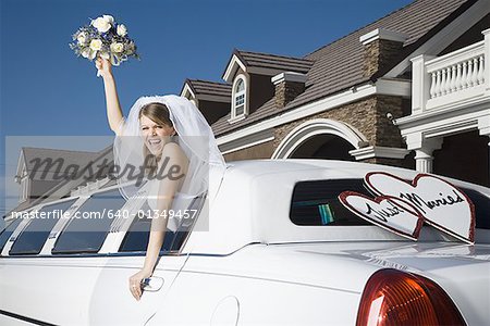 A bride holding a bouquet of flowers and leaning out of a limo window