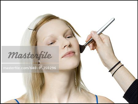 Close-up of a person's hand applying blush on a young woman's face