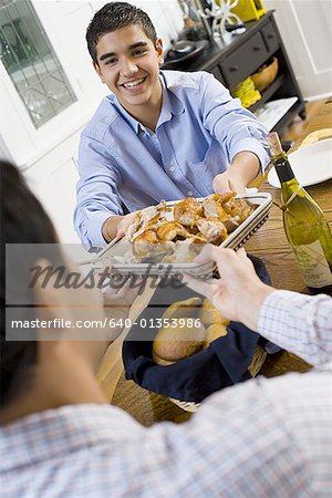 Teenage boy handing a plate of roasted chicken to his father