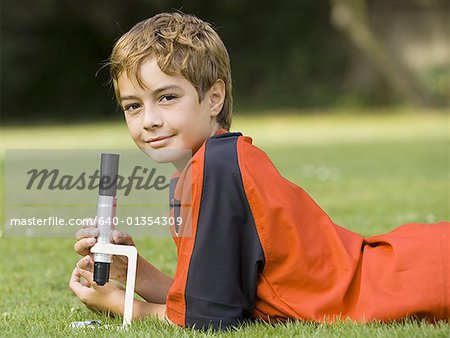 Boy lying down on grass with microscope