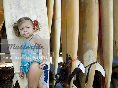 Portrait of a baby girl leaning against a surfboard