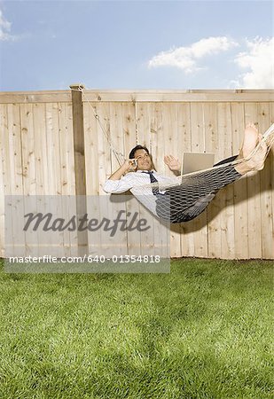 Businessman lying down in a hammock, talking on a mobile phone
