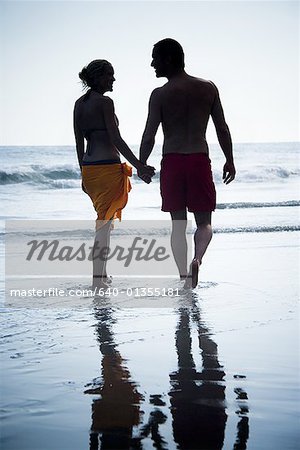 Rear view of a mid adult couple holding hands and walking on the beach