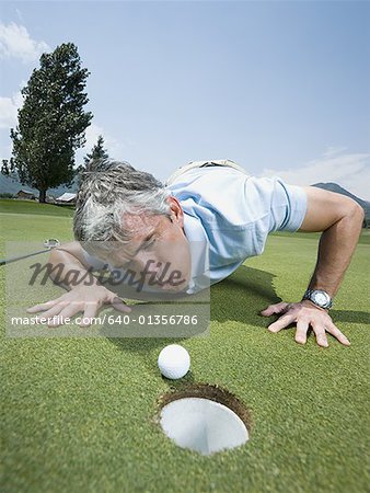 Close-up of a man blowing a golf ball towards a hole
