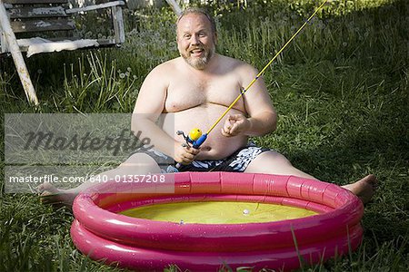 Overweight man in inflatable wading pool - Stock Photo - Masterfile
