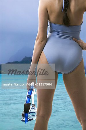 Rear view of a young woman standing holding swimming goggles