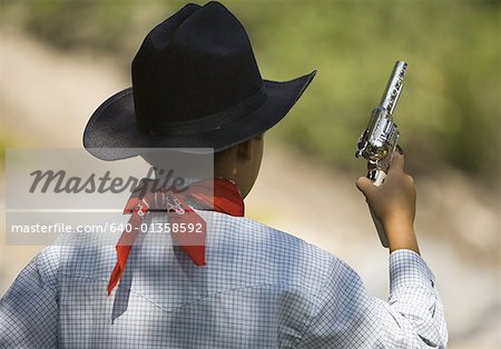 Rear view of a boy in a cowboy costume holding a toy gun