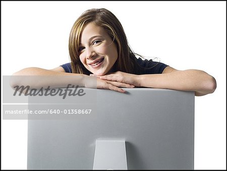 Girl with braces leaning on computer monitor smiling