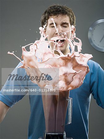 Young man shouting as milk shake spills out of a blender
