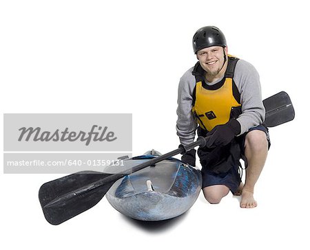 Portrait of a young man kneeling beside a kayak