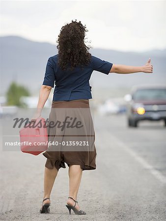 Rear view of a young woman holding a gas can and hitchhiking