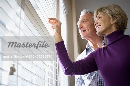 Low angle view of a mature couple looking through blinds of a window
