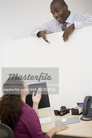 Businessman and a businesswoman talking over cubicle