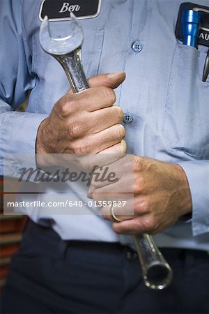 Mid section view of an auto mechanic holding a spanner