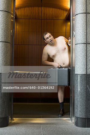 Naked businessman standing in an elevator and holding a briefcase