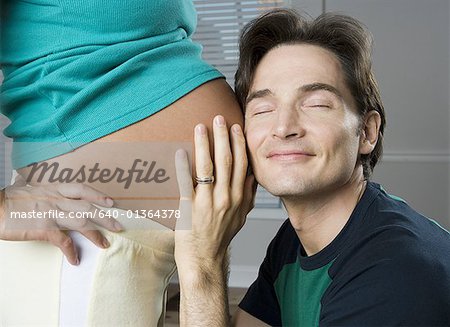 Close-up of a man putting his ear up to a pregnant woman's stomach