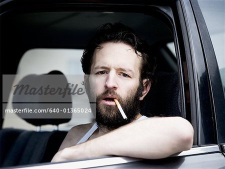 Man in car with cigarette hanging from mouth