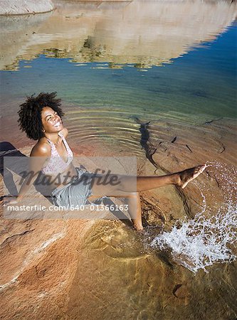 High angle view of a young woman sitting on a rock, splashing water