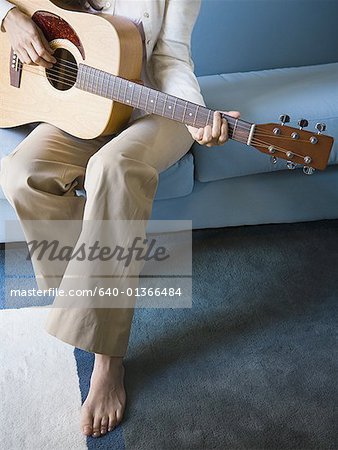 Mid adult woman sitting on a couch playing the guitar
