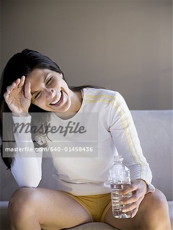 Woman sitting on sofa with bottled water smiling