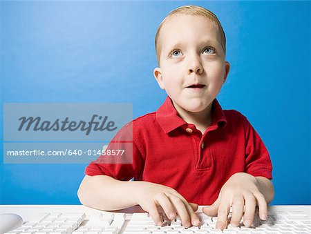 Boy typing at keyboard looking up