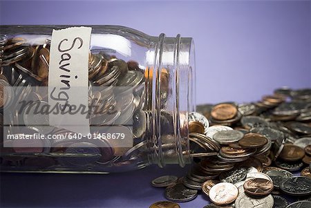 Glass jar with coins and Savings label and scattered coins