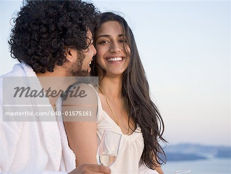 Couple sitting outdoors with champagne flutes and scenic background smiling and snuggling