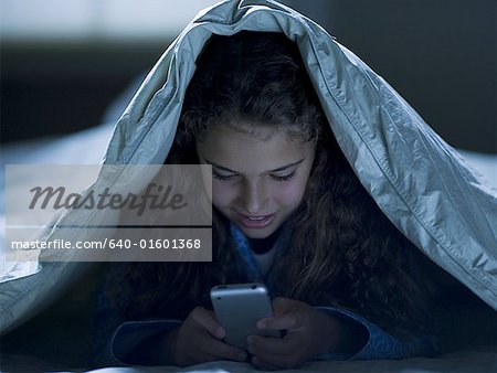 Girl under blankets at night with a smart phone
