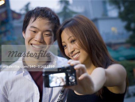 Couple embracing and smiling outdoors with camera