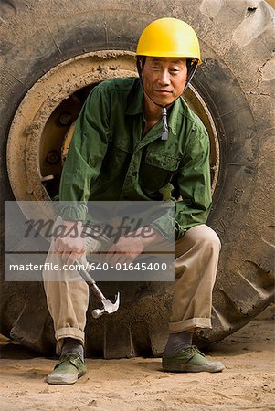 Construction worker sitting on tire of large machine