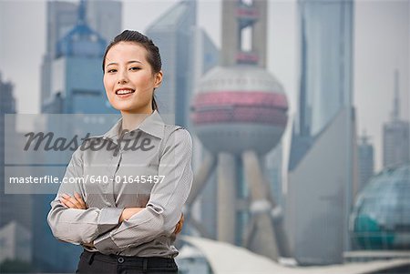 Businesswoman smiling outdoors with arms crossed and city skyline in background