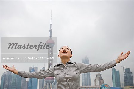 Businesswoman smiling outdoors with arms up and city skyline in background