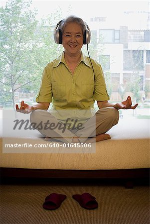 Mature woman sitting cross legged meditating with headphones smiling