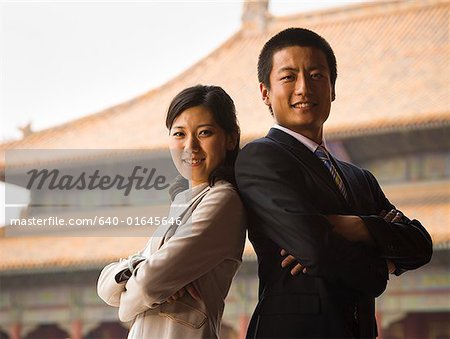 Businessman and woman standing with arms crossed and backs together with pagoda in background