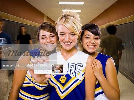 Three High School cheer leaders taking a picture with a mobile phone.