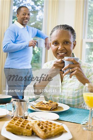 Portrait of a senior woman sitting at the breakfast table with a senior man standing behind her