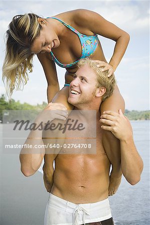 Close-up of a young man carrying a young woman on his shoulders and smiling