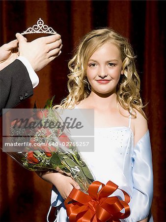 Girl holding red roses being crowned with tiara smiling