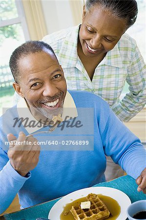 Close-up of a senior man having breakfast with a senior woman behind him