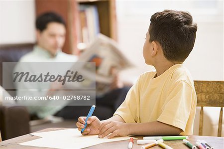 Young boy coloring and drawing with father supervising