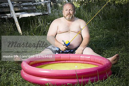 Overweight man in inflatable wading pool - Stock Photo - Masterfile