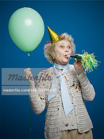 Older woman with noisemaker and party hat - Stock Photo