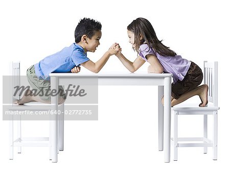 Boy and girl sitting at table arm wrestling