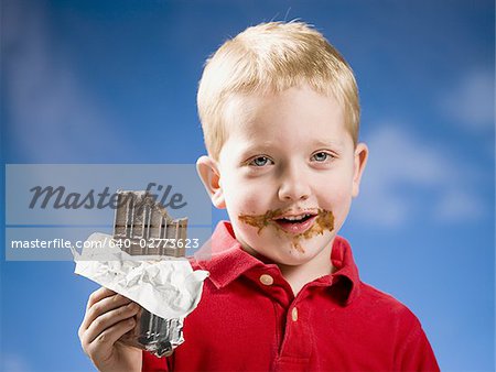 Boy eating chocolate bar with blue sky