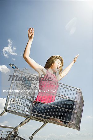 Woman in shopping cart outdoors with arms up smiling