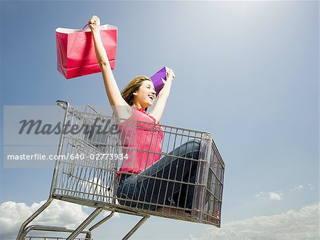 Woman in shopping cart outdoors with shopping bags smiling