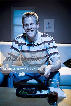Man on sofa with frozen dinner and napkin with food smiling