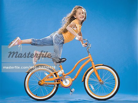 Girl on orange bicycle kneeling on seat with foot up